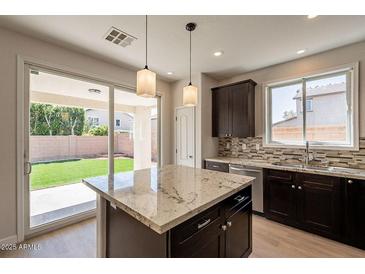 Stylish kitchen showcasing granite countertops, dark cabinets, stainless steel appliances, and access to backyard at 18123 W Lundberg St, Surprise, AZ 85388