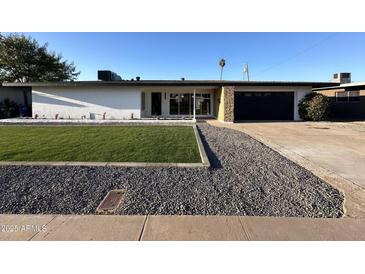 Charming single-story home featuring well-maintained lawn, rock landscaping, and a dark-colored garage door at 1922 W Joan De Arc Ave, Phoenix, AZ 85029