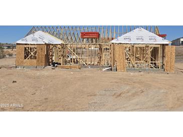 New construction framing shows the home's structure, including studs and roof trusses, in a desert landscape at 1800 W Caramel Ct, Queen Creek, AZ 85144