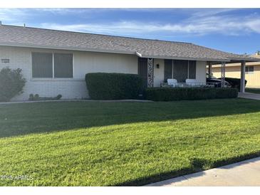 Well-maintained front yard featuring lush green grass, mature landscaping, and a covered porch with outdoor seating at 19046 N Signal Butte Cir, Sun City, AZ 85373