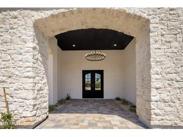 Grand entrance featuring stone archway, black double doors, and decorative chandelier at 7528 E Windrose Dr, Scottsdale, AZ 85260