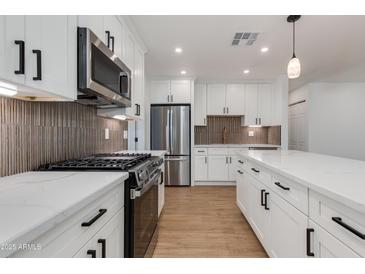 Modern kitchen with stainless steel appliances, gas range, white cabinetry, and a marble countertop island at 7507 E Beatrice St, Scottsdale, AZ 85257