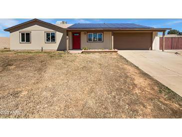 Tan single-story home featuring a red door, two-car garage, and solar panels on the roof at 3702 E Karen Dr, Phoenix, AZ 85032