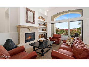 Comfortable living room with a stone fireplace, built-in shelves, and views of the outdoor pool area at 11187 E De La O Rd, Scottsdale, AZ 85255