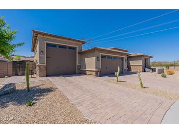 A three-car garage features neutral paint, a brick driveway, and desert landscaping under a clear blue sky at 18159 W Piro St, Goodyear, AZ 85338