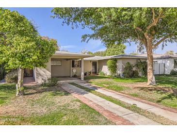 Charming single-story home featuring a well-maintained lawn and a brick-accented driveway leading to a covered carport at 302 E Orange Dr, Phoenix, AZ 85012