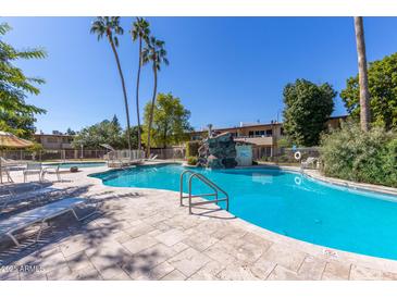 Beautiful community pool surrounded by lounge chairs, lush landscaping, and clear blue skies at 6118 N 12Th Pl # 2, Phoenix, AZ 85014