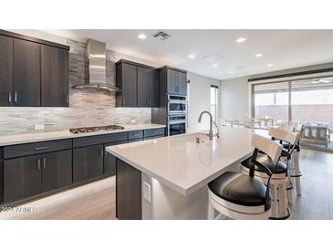 Modern kitchen featuring a large island with seating, stainless steel appliances, and stylish backsplash at 247 E Las Puertas Ln, Queen Creek, AZ 85140
