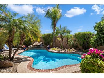 Beautiful pool area with lush landscaping, a rock waterfall, and a sun-drenched patio at 9059 E Butherus Dr, Scottsdale, AZ 85260