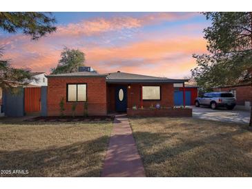 Charming red brick home featuring a well-maintained lawn and an inviting walkway during a colorful sunset at 2511 E Pinchot Ave, Phoenix, AZ 85016