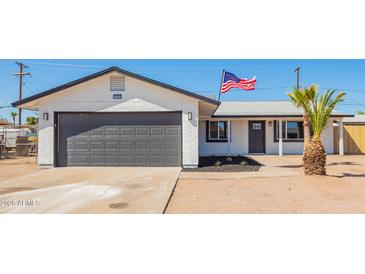 Charming single-story home featuring a gray garage door, desert landscaping, and an American flag waving proudly at 1012 E Estevan Ave, Apache Junction, AZ 85119