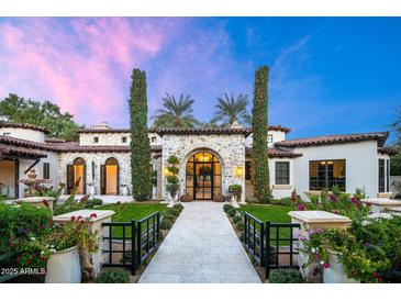 Stunning stone facade with arched entryway, manicured lawn, and lush landscaping creates a welcoming curb appeal at 8601 N 59Th Pl, Paradise Valley, AZ 85253