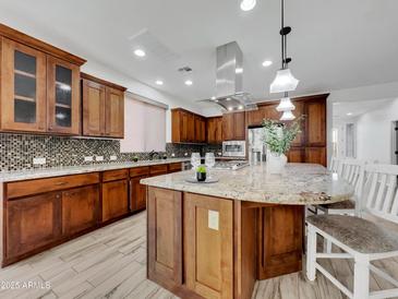Well-equipped kitchen featuring wooden cabinetry, an island, stainless steel appliances and modern lighting fixtures at 77 E Atole Ct, Queen Creek, AZ 85140