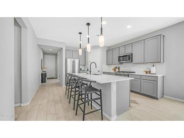 Modern kitchen with gray cabinets, stainless steel appliances, a spacious island with seating, and elegant pendant lighting at 13511 W Cassia Trl, Peoria, AZ 85383