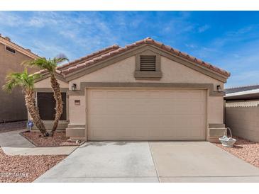 Beige, single-story home featuring a two-car garage, desert landscaping, and a tiled roof against a clear, sunny sky at 11321 W Austin Thomas Dr, Surprise, AZ 85378