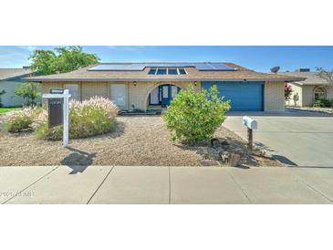 Charming brick home featuring a well-maintained yard, solar panels and a bright blue garage door at 4023 W Joan De Arc Ave, Phoenix, AZ 85029