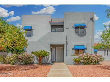 Charming two-story condo featuring blue window awnings and desert landscaping with palm trees and flowering bushes at 220 N 22Nd Pl # 2041, Mesa, AZ 85213