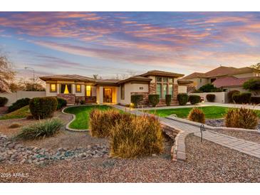 Beautiful single-story home featuring stone accents, a lush lawn, and a charming walkway, all beneath a colorful sunset sky at 911 E Desert Inn Dr, Chandler, AZ 85249