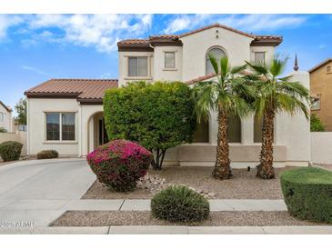 Charming home showcases stucco facade, red tile roof, and lush desert landscaping with palm trees at 16158 W Christy Dr, Surprise, AZ 85379