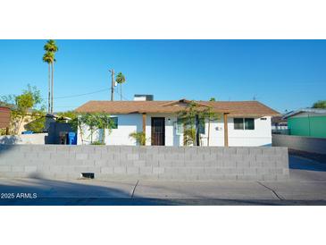 Charming single-story home with a white exterior, brown roof, palm trees, and a block wall in front at 2019 W Wayland Rd, Phoenix, AZ 85041