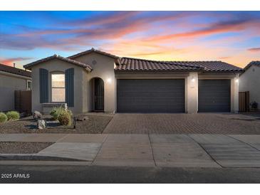 Charming single-story home featuring a three-car garage and desert landscaping under a colorful sky at 22473 E Twilight Dr, Queen Creek, AZ 85142