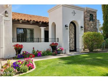 Charming home entrance with a decorative iron gate, well-kept lawn, and vibrant floral accents at 8719 E San Marcos Dr, Scottsdale, AZ 85258