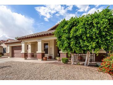 Attractive home showcasing a covered porch area with desert landscaping, mature trees, and a two-car garage at 15328 W Memory Ln, Surprise, AZ 85374