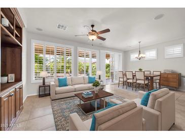Bright living room featuring tan sofas with blue pillows, a ceiling fan and large windows with white shutters at 27614 N 129Th Ln, Peoria, AZ 85383