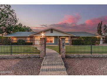 Charming home featuring a brick pathway, iron gate, lush lawn, and mature trees at dusk at 370 E Redfield Rd, Chandler, AZ 85225