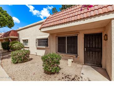 Tan townhome featuring a red tile roof, security bars on windows, and drought-tolerant landscaping at 17242 N 16Th Dr # 6, Phoenix, AZ 85023