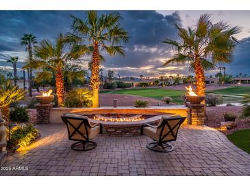 Relaxing outdoor fire pit with chairs surrounded by palm trees and beautiful golf course view at 22912 N San Ramon Ct, Sun City West, AZ 85375