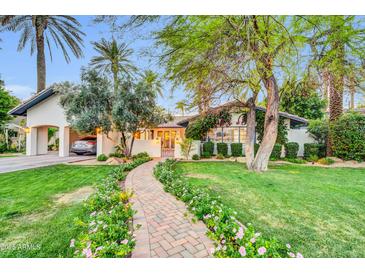 Charming single-story home featuring a brick walkway and beautifully landscaped front yard with mature trees and blooming flowers at 4420 N 47Th Pl, Phoenix, AZ 85018