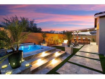 Inviting backyard with a pool, spa, outdoor kitchen, fire pit, and covered patio at dusk at 32268 N 133Rd Ln, Peoria, AZ 85383
