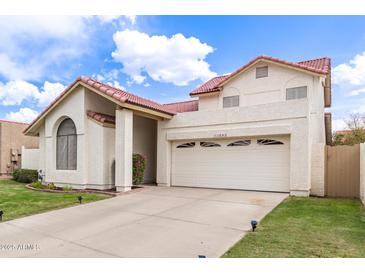 Two-story home with red tile roof, two car garage, well manicured lawn and flower beds at 11243 E Jenan Dr, Scottsdale, AZ 85259