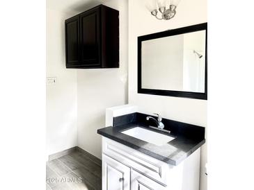 Bathroom with white vanity, black countertop, framed mirror, and dark wall cabinet at 2925 N 19Th Ave # 97, Phoenix, AZ 85015