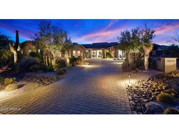 Inviting home exterior with desert landscaping, a paver driveway, and warm exterior lighting at dusk at 39254 N 104Th Pl, Scottsdale, AZ 85262