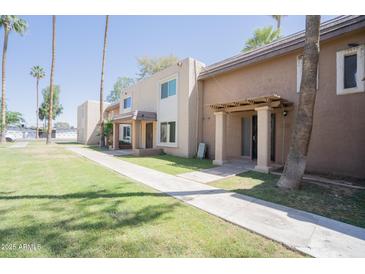 A tan, two-story apartment complex with palm trees and green lawn under a clear blue sky at 7126 N 19Th Ave # 122, Phoenix, AZ 85021