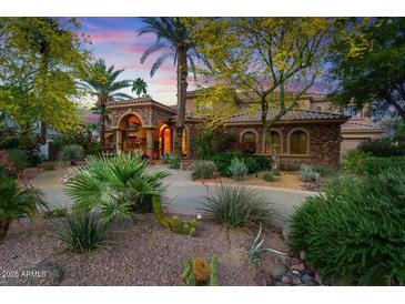 Stunning home featuring lush desert landscaping, a circular driveway, and stone accents under a colorful sunset sky at 11821 S Tuzigoot Ct, Phoenix, AZ 85044