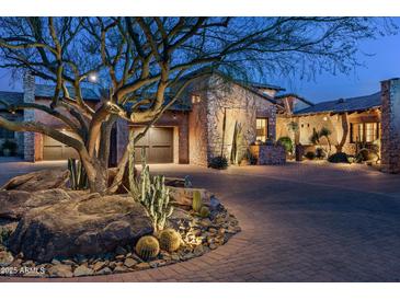 Elegant desert home with stone accents, lush landscaping and a circular driveway at twilight at 10057 E Blue Sky Dr, Scottsdale, AZ 85262