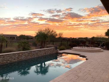 Stunning pool with beautiful sunset reflection, stone trim, and lounge area at 27083 W Marco Polo Rd, Buckeye, AZ 85396