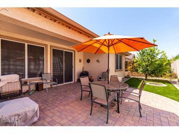 Relaxing back patio featuring a brick floor, comfortable seating, and an orange umbrella for shade at 22940 W Desert Bloom St, Buckeye, AZ 85326
