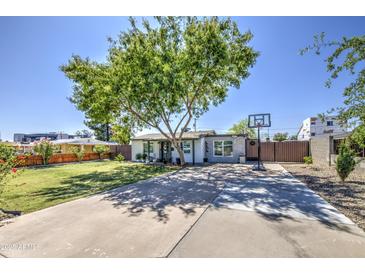 Home featuring a basketball hoop on the driveway, complemented by a lush front lawn and mature tree at 6728 N 24Th Dr, Phoenix, AZ 85015