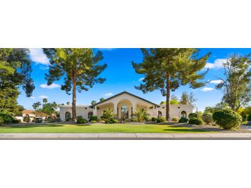 Inviting single-story home with arched entryway, lush landscaping, and mature trees enhancing its curb appeal at 10025 E Larkspur Dr, Scottsdale, AZ 85260