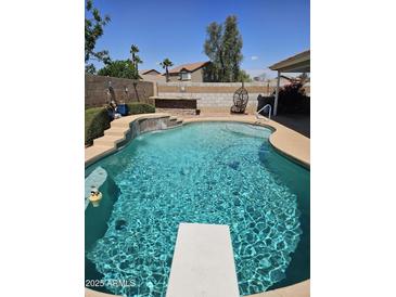 Backyard pool featuring a diving board, rock waterfall, brick surround, and desert landscaping at 11760 N 153Rd Ave, Surprise, AZ 85379