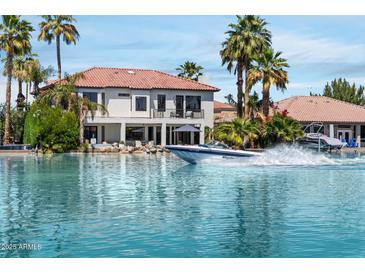 Waterfront backyard with a boat speeding across the lake in front of a Spanish-style home with palm trees at 1539 W Laurel Ave, Gilbert, AZ 85233
