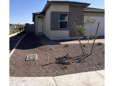 Well maintained single Gathering home featuring a xeriscaped front yard with a small tree, and gray brick accents at 18225 W Larkspur Dr, Goodyear, AZ 85338
