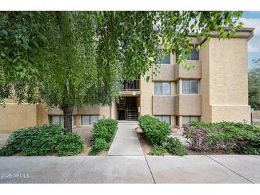 Inviting exterior view of a stucco apartment building entrance with mature trees and manicured landscaping at 18811 N 19Th Ave # 2020, Phoenix, AZ 85027
