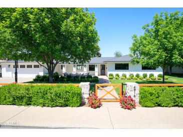 Charming single-story home with a manicured lawn, wood fence, and mature trees in a suburban neighborhood at 4916 E Flower St, Phoenix, AZ 85018