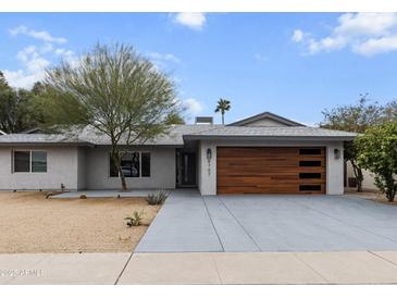 Charming single story home with desert landscaping, gray stucco, and a modern wood grain garage door at 8707 E Clarendon Ave, Scottsdale, AZ 85251