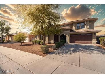 Inviting two-story home with a well-manicured lawn, mature trees, and a two-car garage and warm sunset at 18640 W Pioneer St, Goodyear, AZ 85338